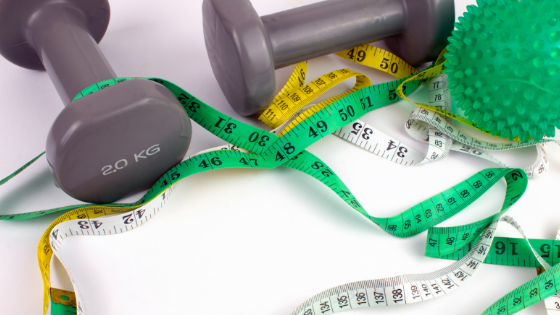 Two gray dumbells, a green ball, and green, yellow, and white tap measures on a white background.