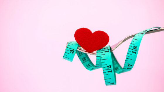 Silver fork wrapped in a turquoise tape measure, with a red felt heart, on a light pink background.