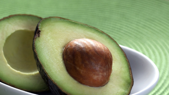 One avocado cut in half in a white bowl on a green background.