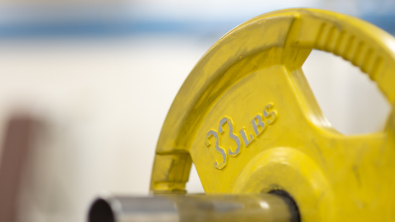 A bright yellow barbell plate with the words "Strength Training 101: What To Do At the Gym" in black.