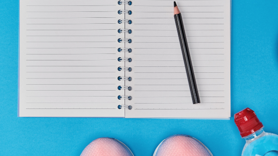 White notebook on bright blue background with the very tips of pink sneakers and a bottle of water.