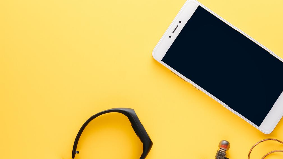 Yellow background with a white phone, black watch, and black earbuds in the right corner.