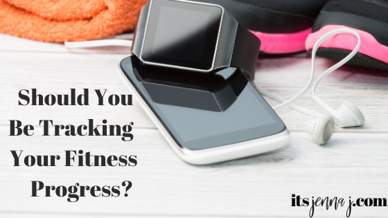 A light grey background with an orange rolled up towel, black and pink sneakers, a black and white phone, a black watch, and white headphones. "Should You Be Tracking Your Fitness Progress" in black text. 