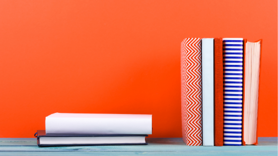 Multi-colored books on a gray table against a bright orange wall.