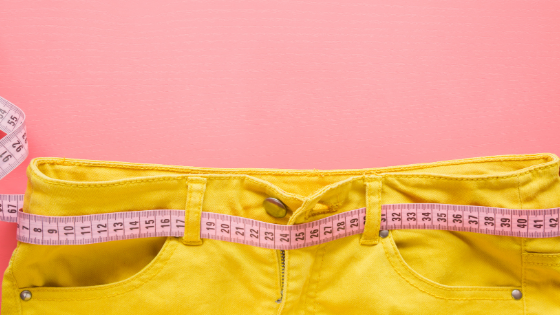 Light pink background with yellow jeans and a pink tape measure looped through the belt loops.