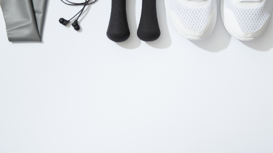 White sneakers, black weights, headphones, and a gray resistance band line the top of a while background.