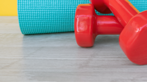 Bright Blue Yoga Mat With Red Weights On A Grey Floor And A Bright Yellow Background