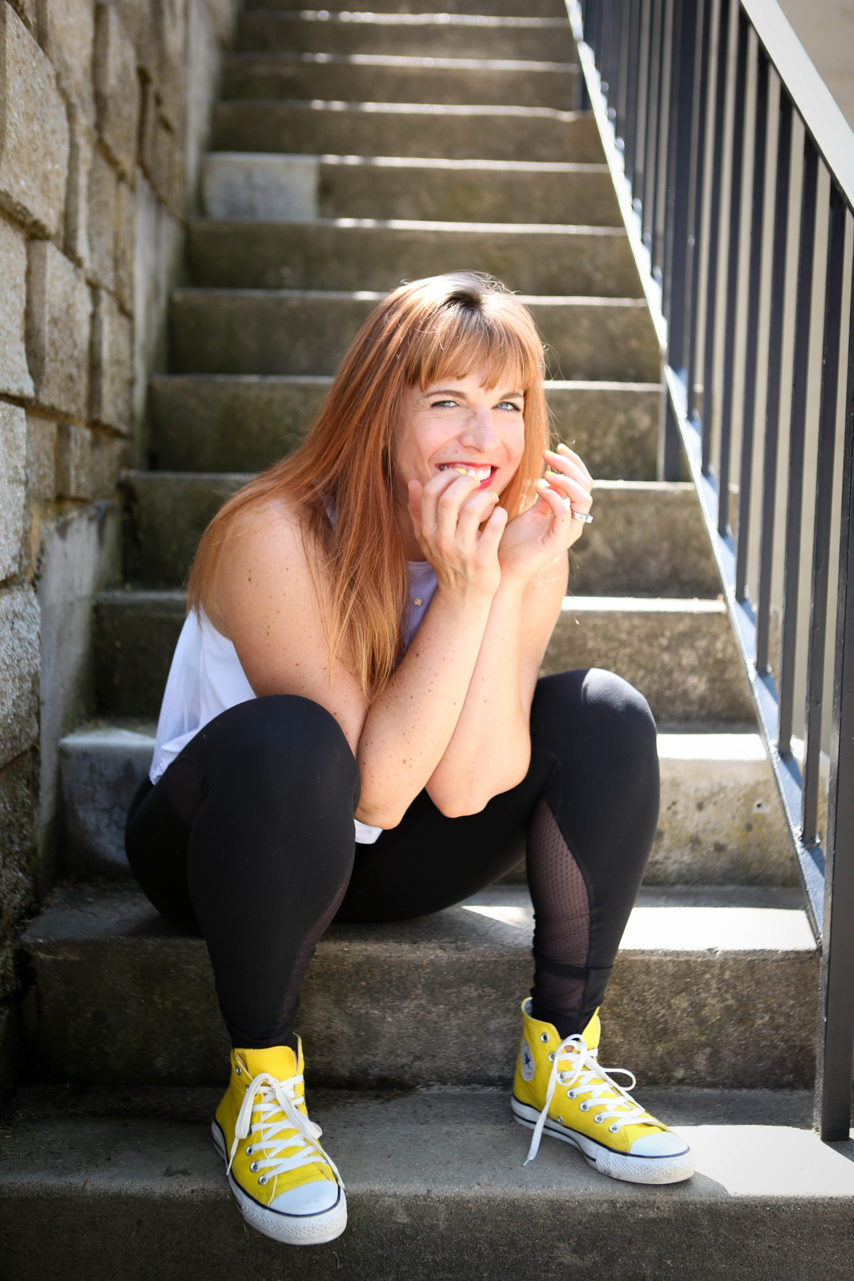 Jenna sitting at the bottom of concrete steps, smiling with her hands in front of her face.